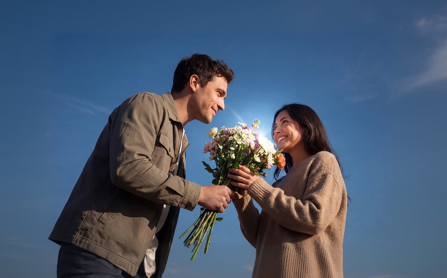 Person überreicht einen bunten Blumenstrauß unter blauem Himmel