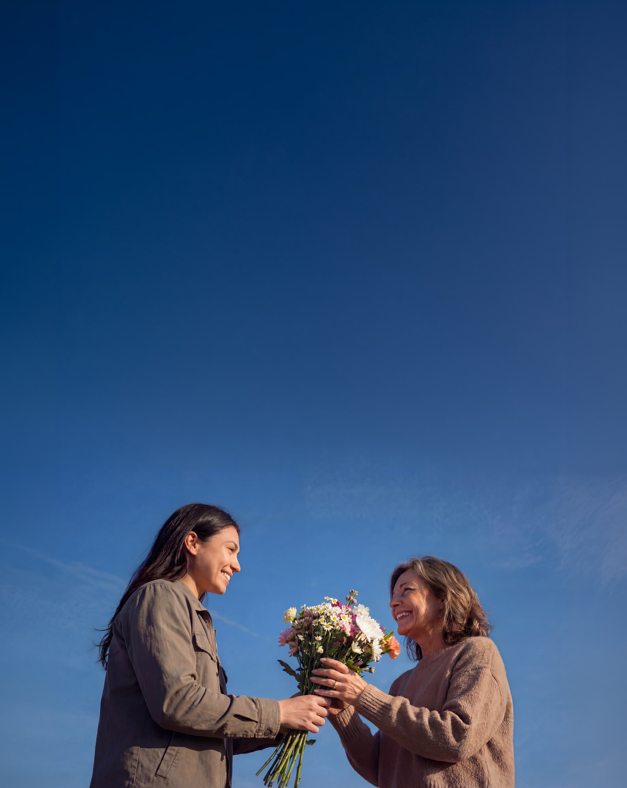 Zwei Personen mit einem Blumenstrauß vor blauem Himmel