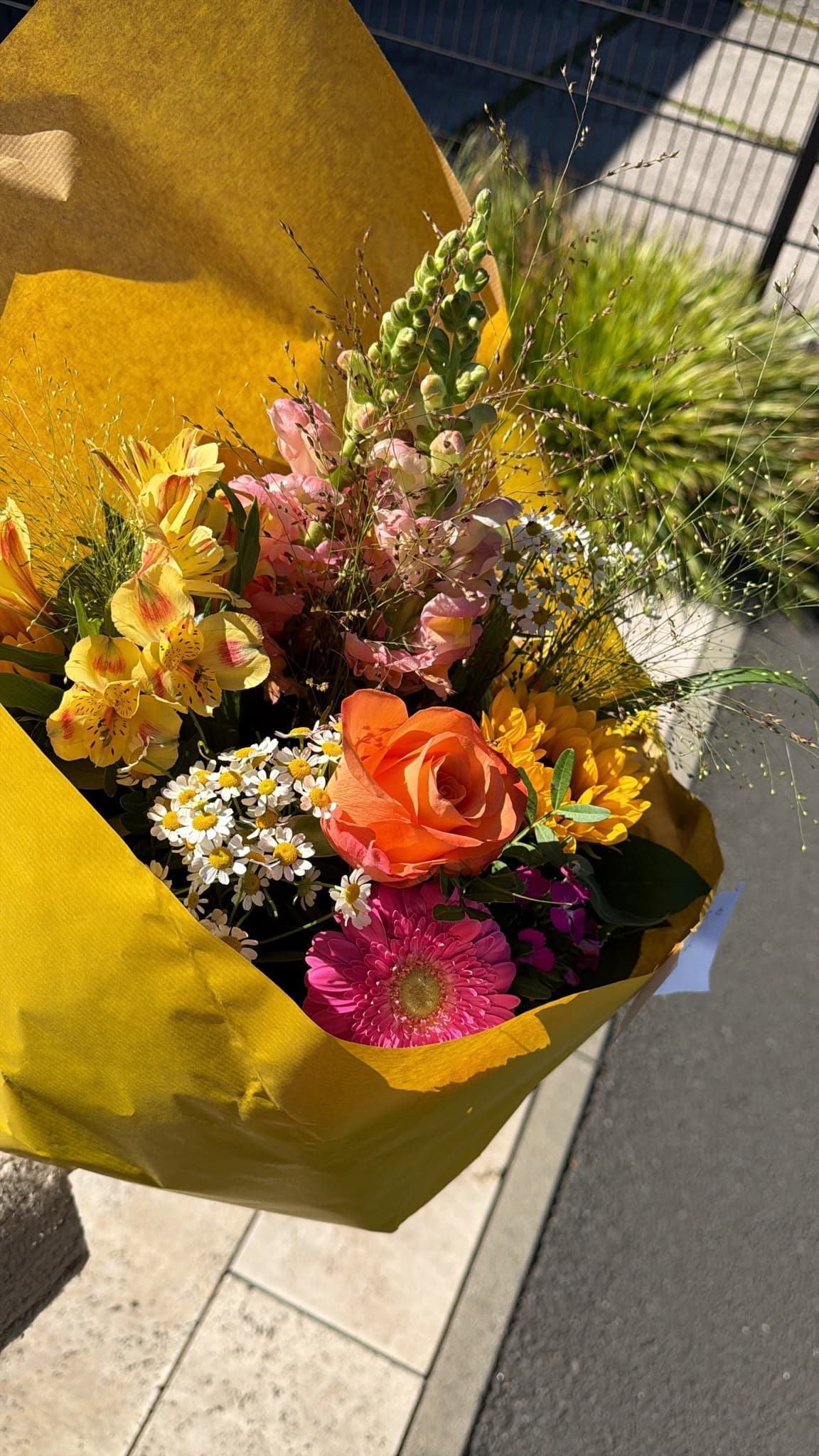 Farbenfroher Blumenstrauß in gelbem Papier mit Rosen, Gerbera, Ranunkeln, Gräsern und weißen Blüten