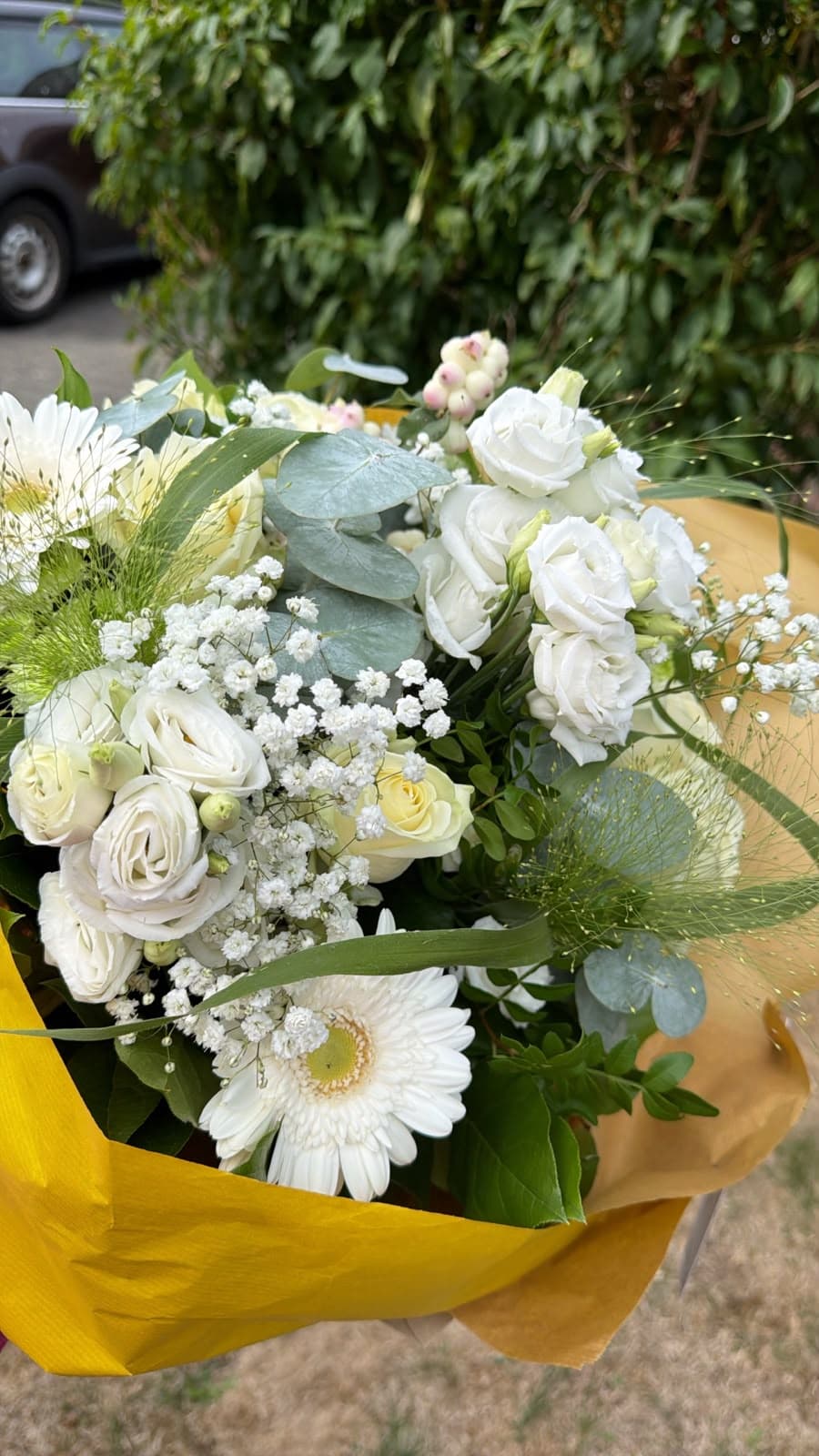 Blumenstrauß mit weißen Rosen, Gerbera, zartem Schleierkraut, Eukalyptus und rosa Akzenten in gelbem Papier