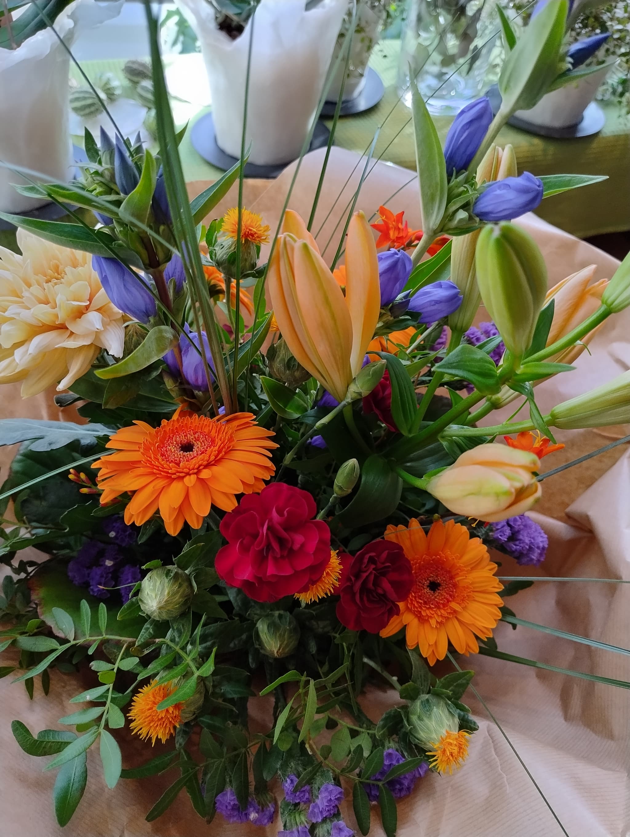 Bunter Blumenstrauß mit orange Gerberas, roten Rosen, lila Lisianthus, peachy Dahlien und Grünwerk in weißer Vase